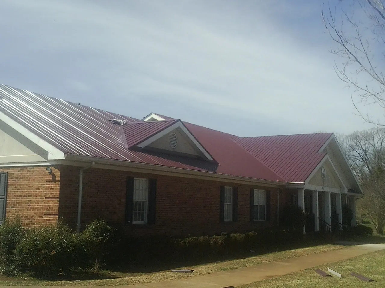 Red metal roof with gabled entries on a long brick building, from a Hail Damage Roof Repair job in Oakfield