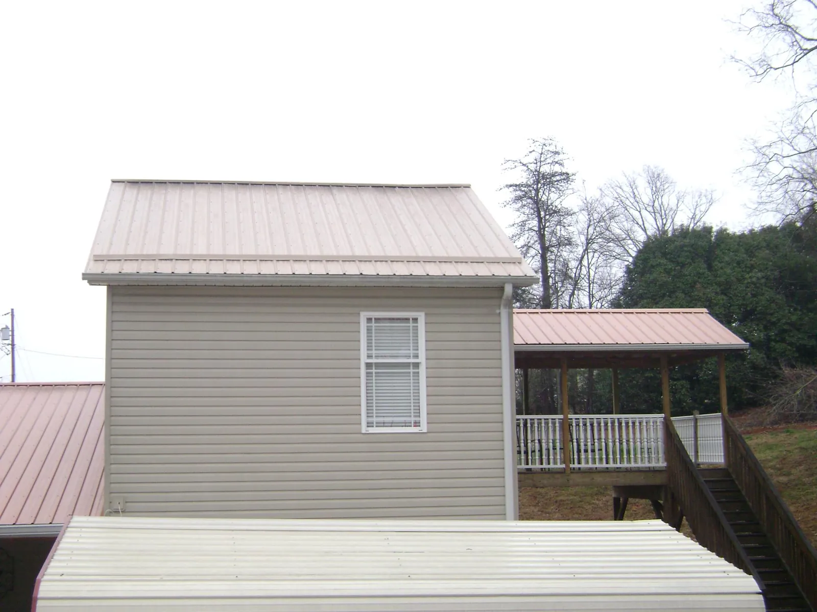 Tan metal roofs on a two story addition and attached porch, from a Roof Replacement job in Oakfield